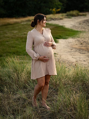 Schwangere Frau steht seitlich zur Kamera und schaut seitlich an der Kamera vorbei