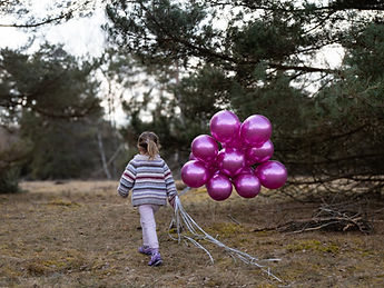 Kind mit gestreiftem Pulli läuft mit pinkfarbenen metallic Luftballons vom Fotografen weg