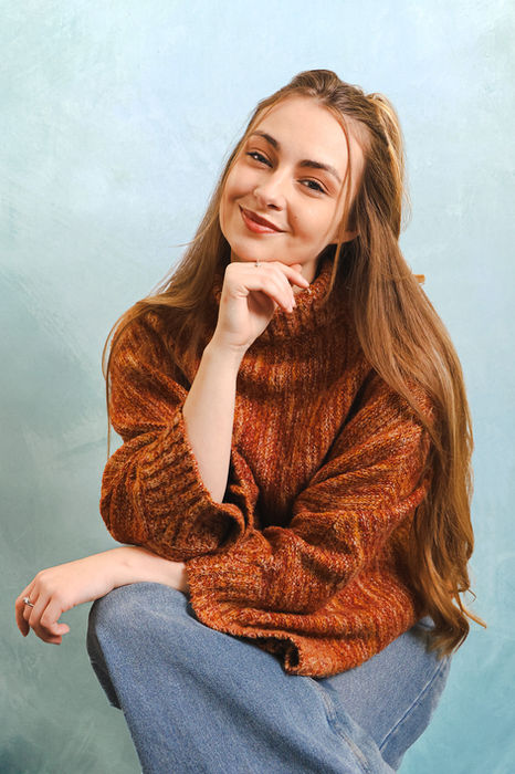 A seated portrait of a woman wearing a brown jumper, photographed in a relaxed pose at a London studio, ideal for creatives, artists, or personal brand storytelling.