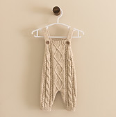 Cable knit overalls for a newborn hang against a wall.