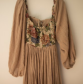 Tan dress with puff sleeves and a floral tapestry bodice hands against a wall