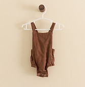 A brown linen onesie hangs against a wall.