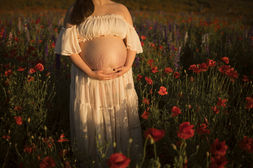 Pregnant woman holds her belly in a field of red poppies photographed by Raleigh maternity photographer.