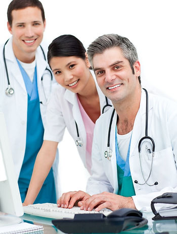 Three smiling medical professionals with stethoscopes standing at a computer