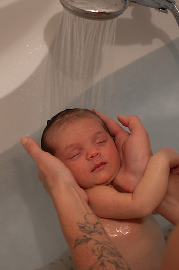 Bain thérapeutique : un bébé apaisé tenu par une professionnelle de soin sous un filet d’eau tiède