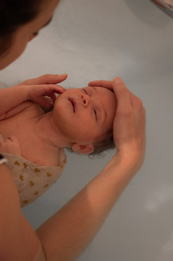 Nouveau-né bercé par une professionnelle de soin, lors d’un bain thérapeutique, ambiance apaisante.