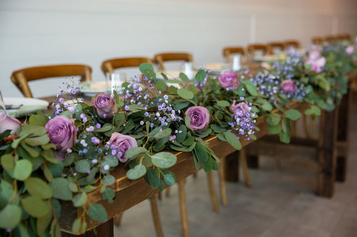 Long reception table with purple floral garland and wooden chairs in Alberta venue.