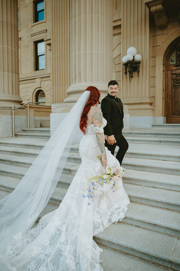 Bride posing with long flowing veil on grand stone staircase.