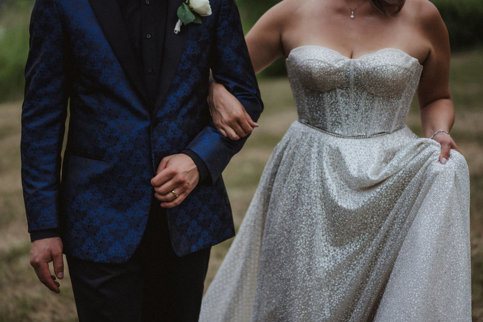 Detail of groom’s navy suit and bride’s shimmering gown at outdoor ceremony.
