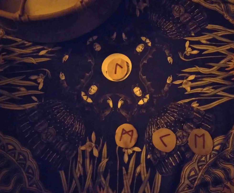 On the background of a cloth showing women dressed as bats, we see runes - Laguz at the top, Mannaz, Kenaz, and Ehwaz underneath.