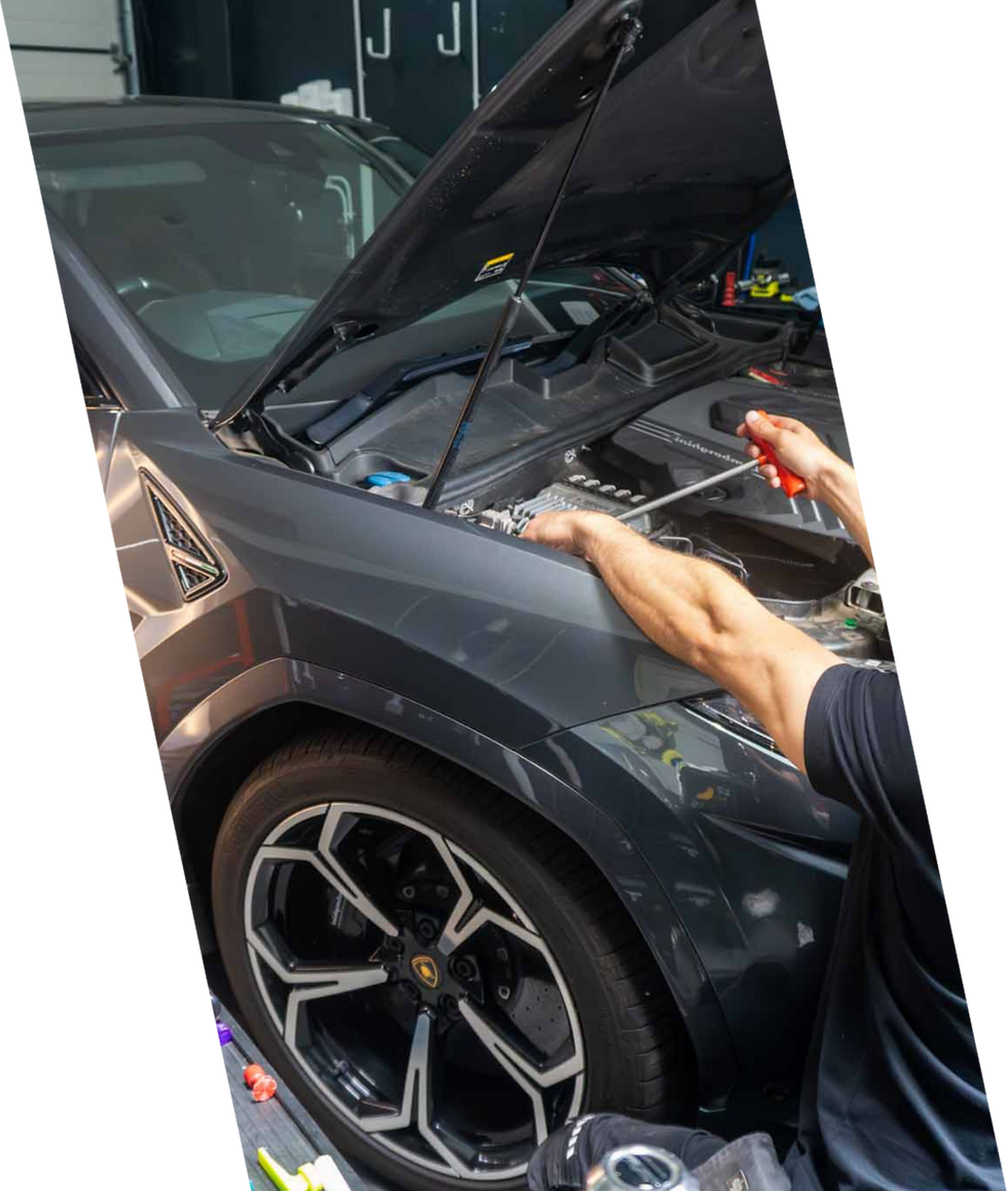 Mechaniker arbeitet mit Werkzeug am Motor eines grauen Sport-SUVs bei geöffneter Motorhaube.png