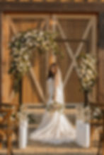 An elegant bride standing in front of the main barn doors taking outside wedding photos