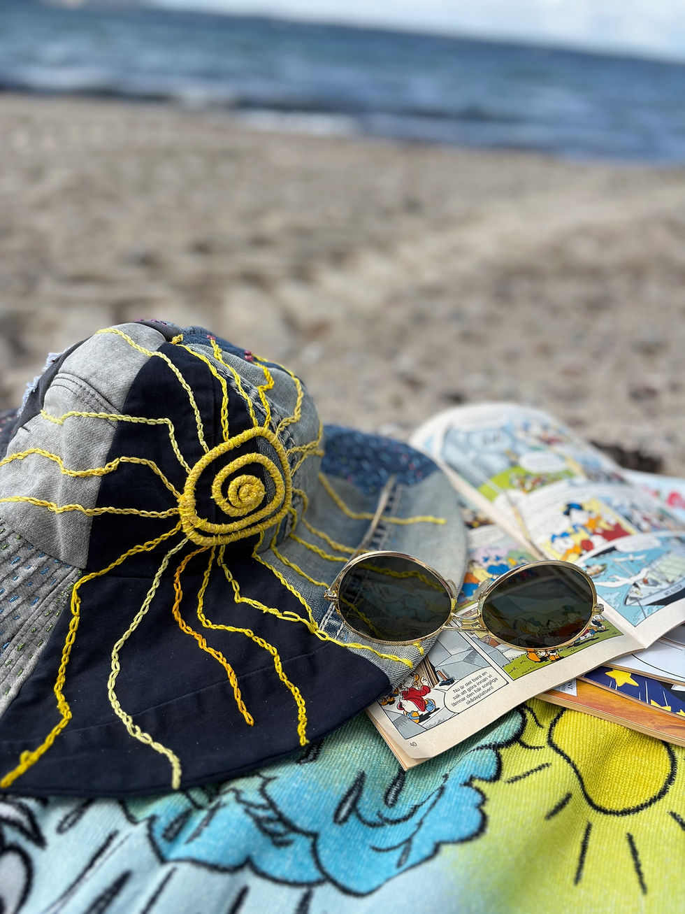 Hatt på stranden med broderad sol på stranden med hav och sand.