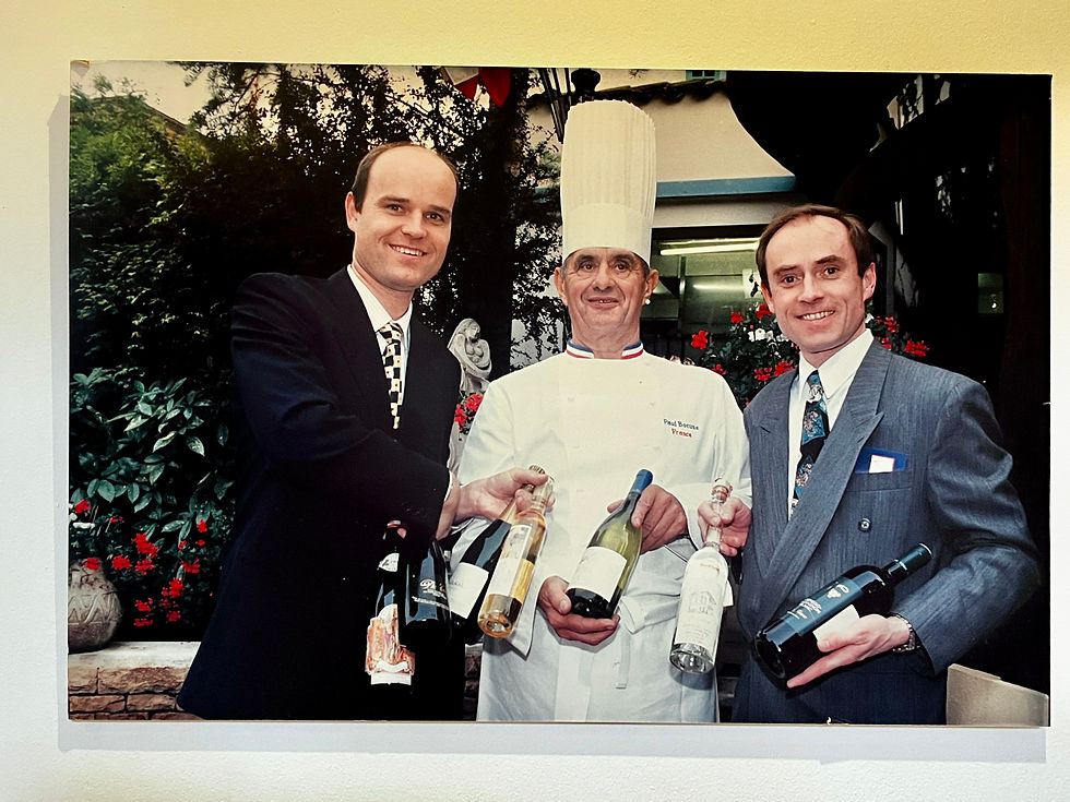Rudi (links) und Karl Obauer (rechts) mit dem legendären französischen Chef Paul Bocuse auf einem Foto, das im Stiegenaufgang ihres Hotels prangt.