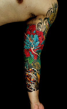 Vibrant Japanese-style sleeve tattoo featuring bright red and turquoise peony flower with green leaves, colorful waves, and traditional ornamental patterns on dark background, extending from shoulder eo elbow with bold color saturation and clean black outlines.