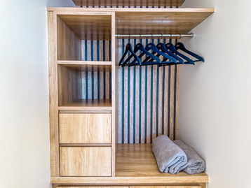 Open light wood closet with hanging space, hangers, shelves and folded towels in a villa in Paradise Bay