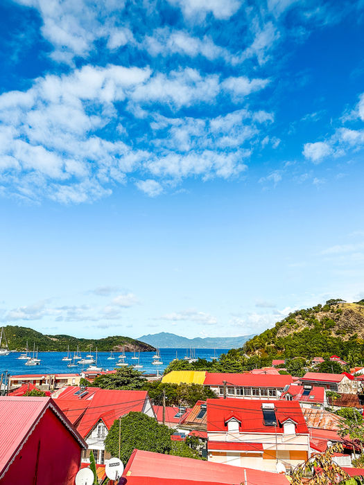 Panorama du village de Terre-de-Haut avec ses toits rouges, la baie des Saintes et les bateaux au mouillage sous un ciel bleu