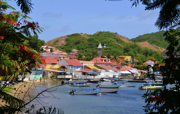 Vue panoramique du bourg de Terre-de-Haut aux Saintes, avec ses maisons colorées, son port animé et ses eaux turquoise, offrant un cadre pittoresque et typique des îles de la Guadeloupe.