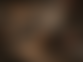 Close-up of weathered hands holding a steaming cup of herbal tea in a medieval tavern. The dark ceramic mug contains coltsfoot tea, with gentle steam rising. Rough wooden tables, loaves of bread, and cloths surround the scene, while blurred figures sit by candlelight in the background, capturing a moment of everyday medieval healing and tavern life.