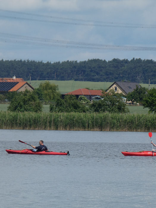 Zwei Personen in roten Kajaks auf einem ruhigen See.