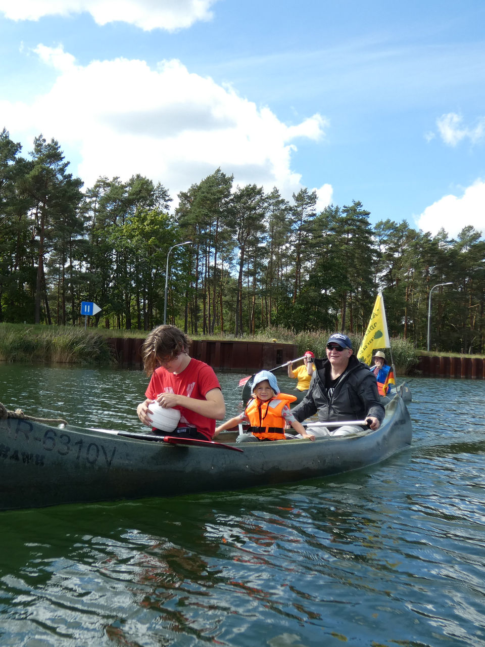 Familie bei einer Kanutour auf einem von Bäumen gesäumten Fluss.