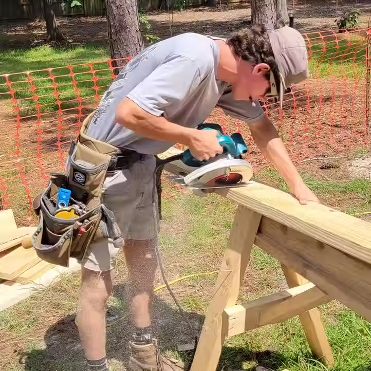 Carpenter using a circular saw on a wood beam outdoors