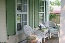 White wicker chairs on a porch with green shutters.