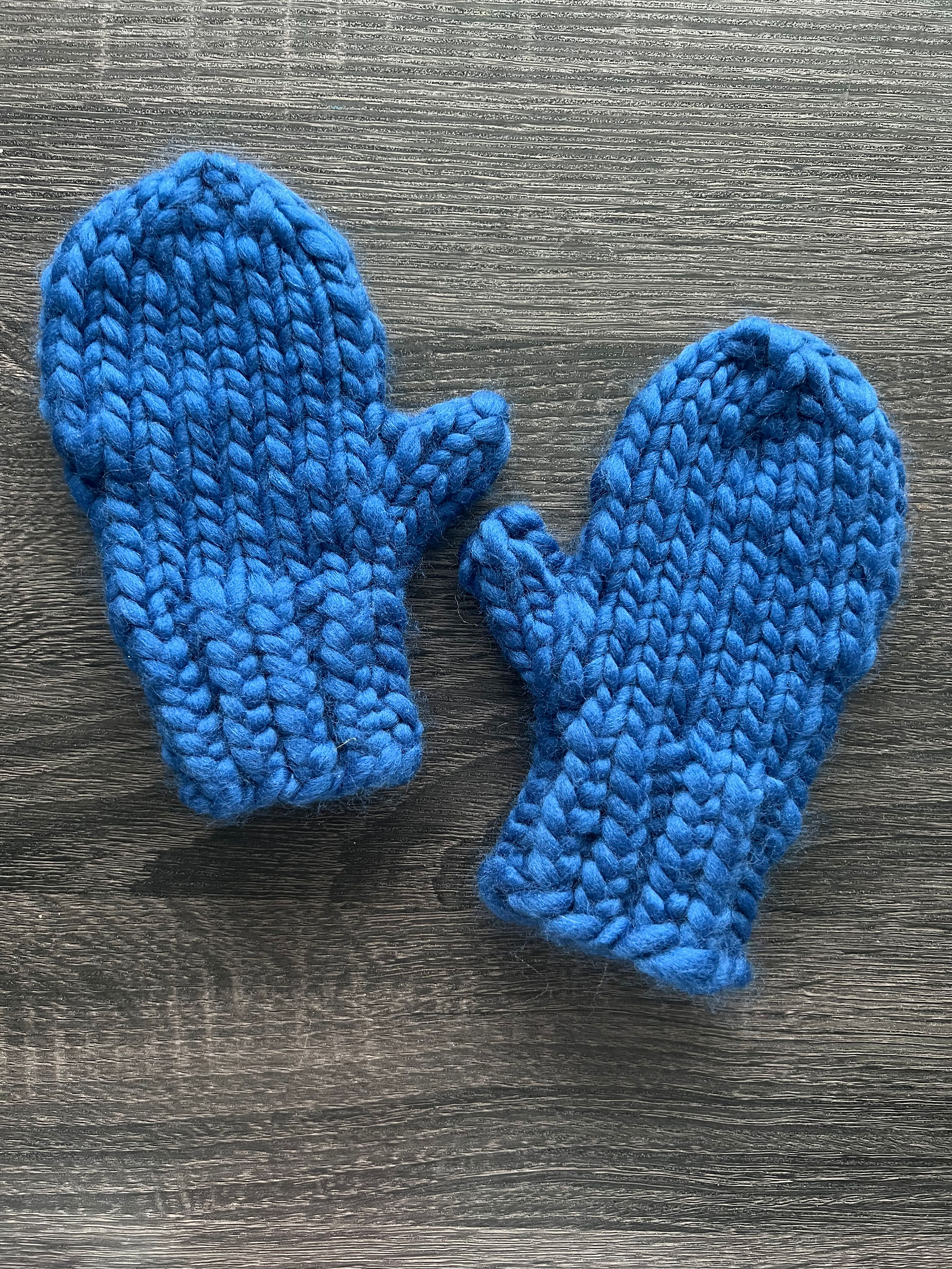 Super cozy plain knit blue mittens sit on a wooden surface.