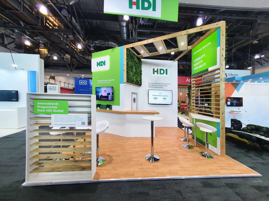 Custom sustainable exhibition stand for HDI Global at Airmic 2022. The reusable exhibition stand features a digital display, biophilic design, slat walls and branded graphics.