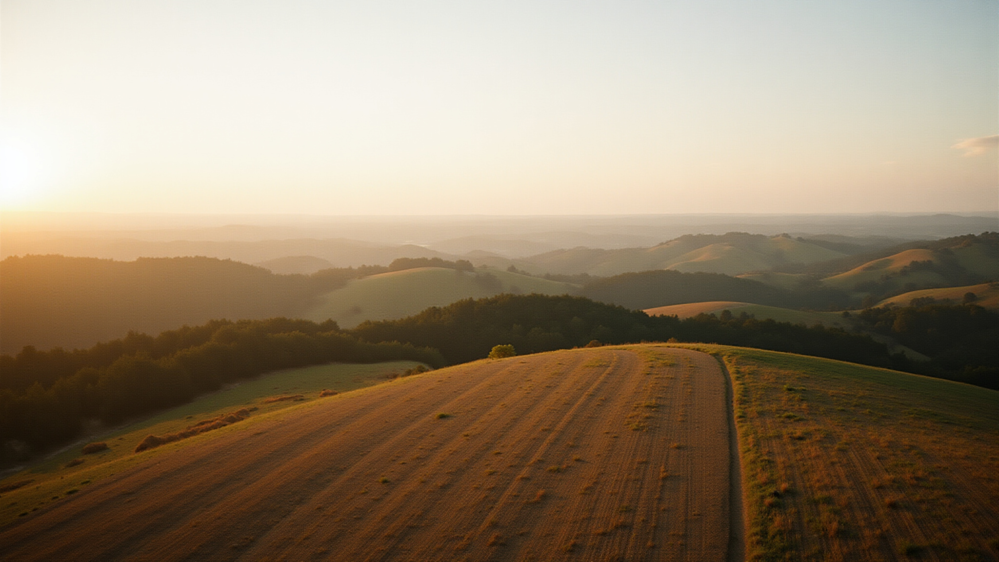 Golden sunset over rolling hills and cultivated field landscape.