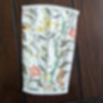 Flatlay photo of a stomacher on a wood table. Stomacher is slightly rectangular in shape with botanical garden floral print of yellow, white and red long stem flowers. Finished at top and bottom with white binding to match the corset.