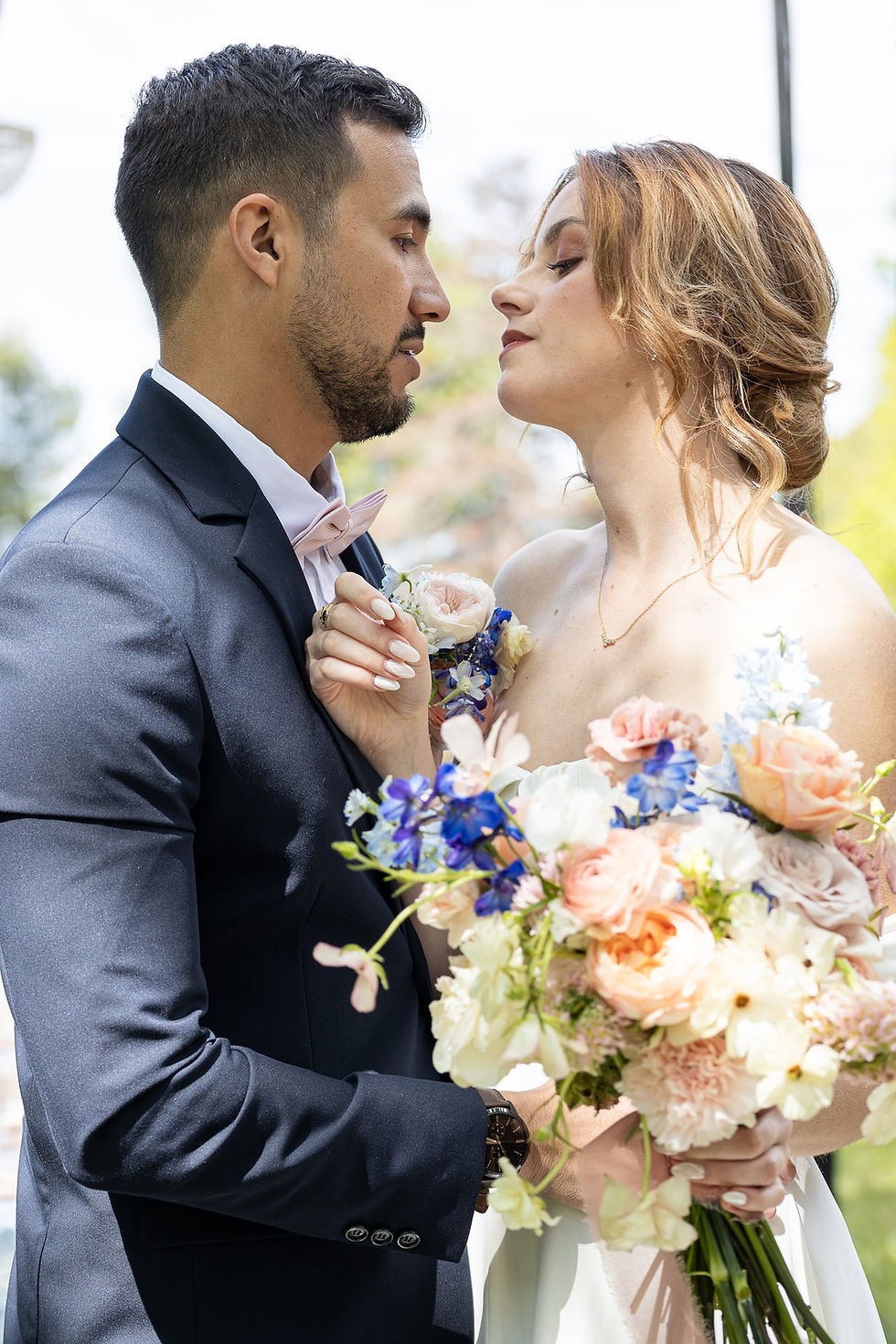 Bouquet de mariée aux roses pêche et fleurs bleues, entre les mains du couple