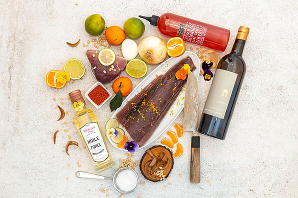 Photographie culinaire en flatlay d’un plat de poisson, agrumes, épices et bouteille de vin