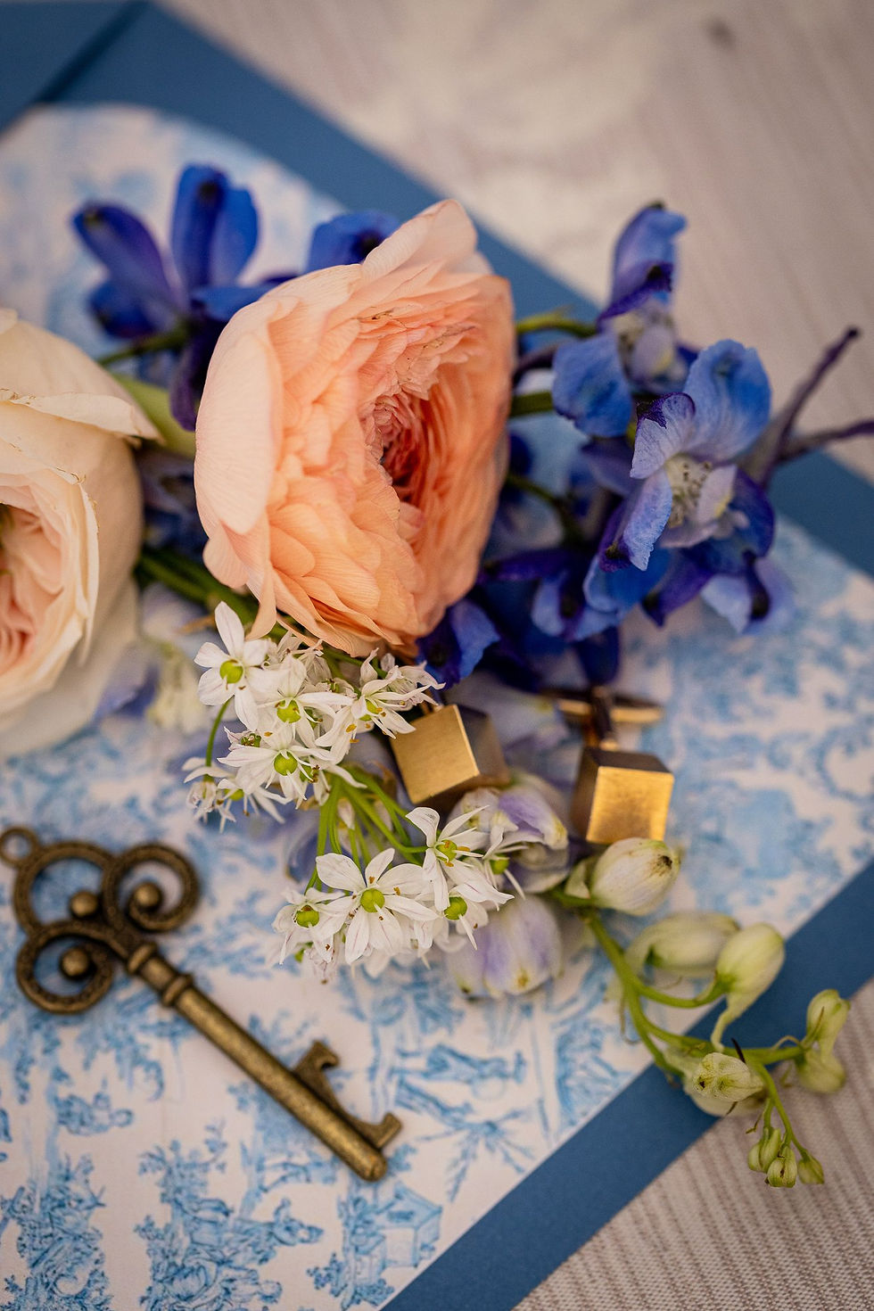 Détails de mariage : clé ancienne, rose pêche et fleurs bleues sur une toile de Jouy