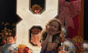 Girl celebrating her 8th birthday with large light up number with neon and tassel backdrop.