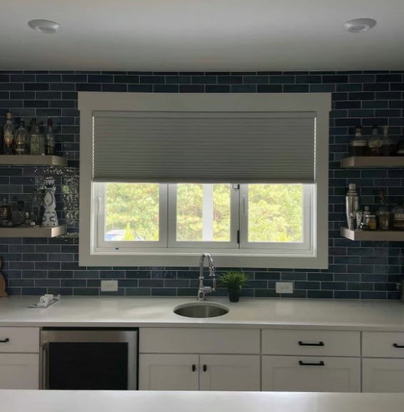 White blackout cellular shades in the mid-way down position over a kitchen sink.