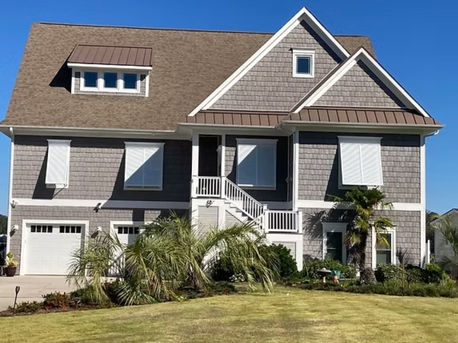 Coastal white, impact Bahama shutters with matching behind mounted support arms installed on a naturally aged cedar shake beach house with white trim.