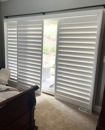 Bedroom with outside mounted, sliding 3 1/2" hybrid clear-view shutters over a sliding glass door in a painted finish.