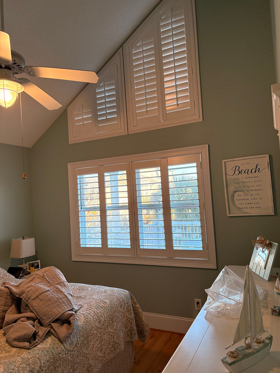Cozy bedroom with a calming beach theme, featuring Plantation Shutters over a triangular shaped window above and rectangular windows below.