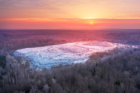 A bright red sunrise over a large wild forest in which the city's trash can is a landfill