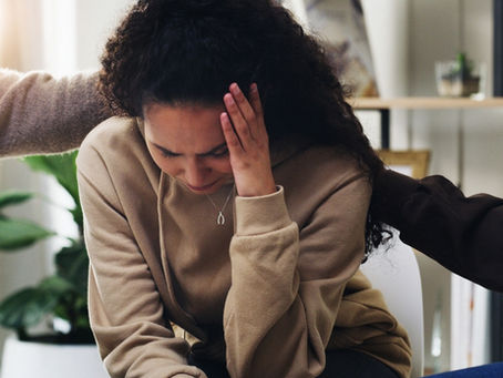 A woman sits in distress from her trauma while two people attempt to comfort her