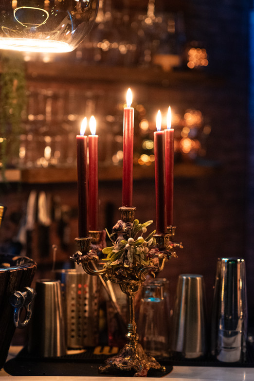 Golden baroque candleholder with five dark red candles on the bar counter, with wine glass shelves blurred in the background.
