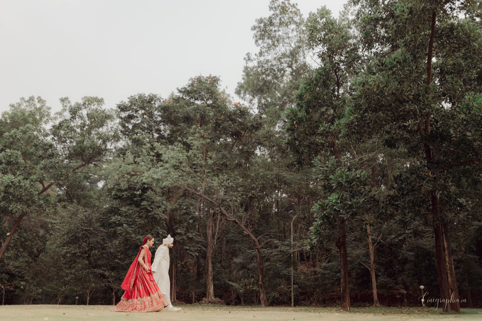 Couple in red and white wedding attire walking in woods.