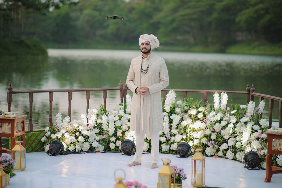 Man in cream sherwani and turban by a lake with white flowers