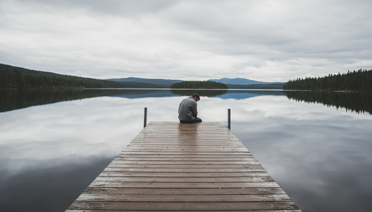 Wide-angle view of a person sitting alone on a quiet lakeside dock