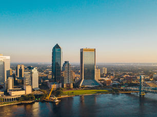 Downtown Jacksonville skyline at sunset with TIAA Bank and Wells Fargo towers, bridge over the river, calm water below.
