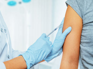 Healthcare worker in blue gloves giving an injection in a patient’s upper arm in a bright clinic, close-up with no visible text