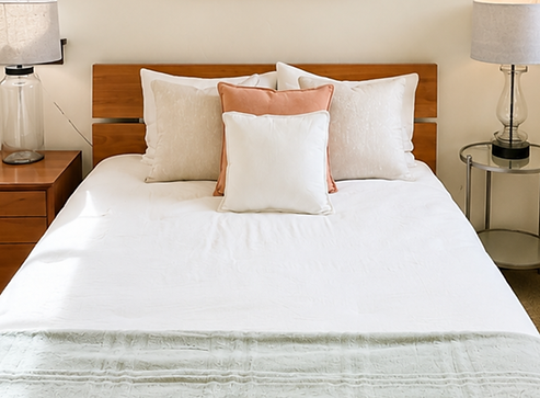 Close-up of staged bed with wood headboard, white and terracotta pillows, and sage green quilt