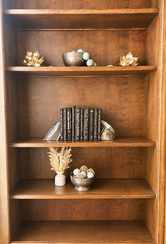 Wood bookshelf at Wellington styled with gold leaf decor, a ceramic bowl, stacked books with bookends, and a small vase with dried florals.