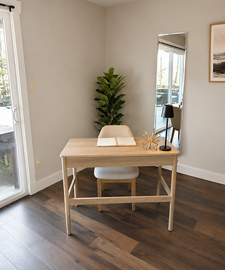 Staged corner desk at Deer Path with a light wood desk and cream upholstered chair, an open book and gold star-shaped decor on top, a fiddle leaf fig plant, a tall leaning mirror, a black table lamp, and dark hardwood flooring.